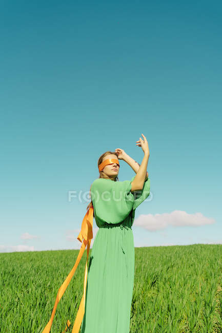 Jovem de olhos vendados usando um vestido verde de pé em um campo — Fotografia de Stock