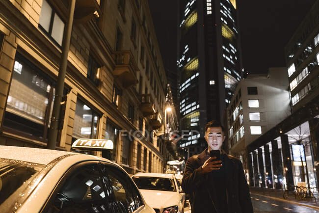 Homem usando smartphone enquanto caminha na cidade à noite — Fotografia de Stock