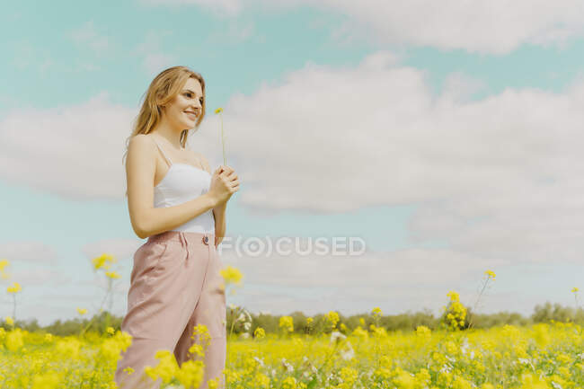 Giovane donna in piedi in un prato in primavera con un fiore in mano — Foto stock