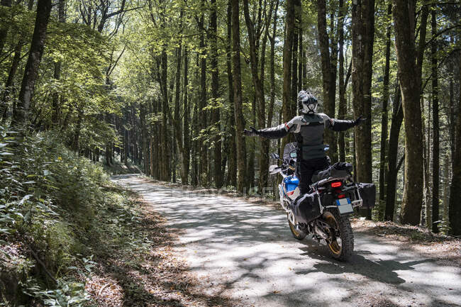 Motociclista em uma viagem em uma estrada florestal com os braços estendidos — Fotografia de Stock