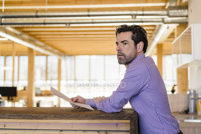 Empresario sosteniendo papeles en oficina abierta de madera - foto de stock