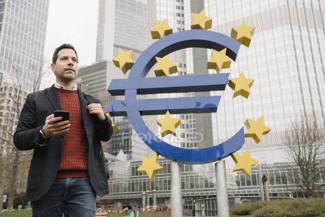 Empresário atencioso que usa o telemóvel enquanto se opõe à escultura e ao Banco Central Europeu — Fotografia de Stock