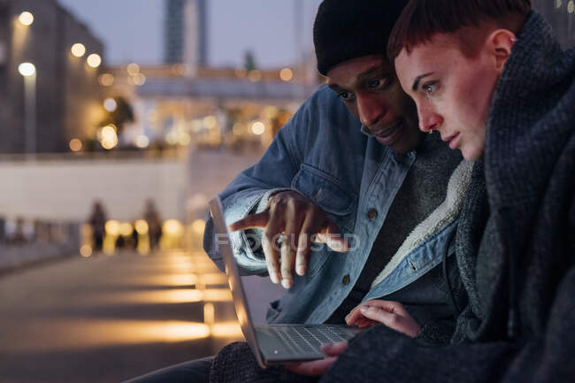 Щаслива молода пара використовує ноутбук у місті в сутінках — стокове фото