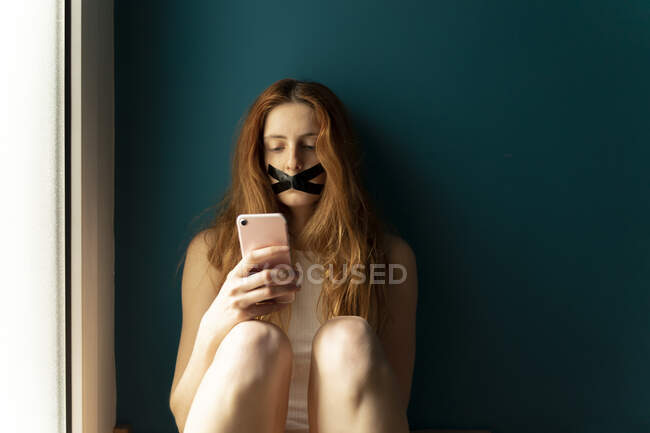 Молода жінка з пристебнутим ротом за допомогою мобільного телефону. — стокове фото