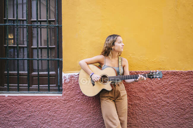 Молода жінка, яка грає на гітарі, стоячи навпроти стіни, Санта - Крус (Севілья, Іспанія). — стокове фото