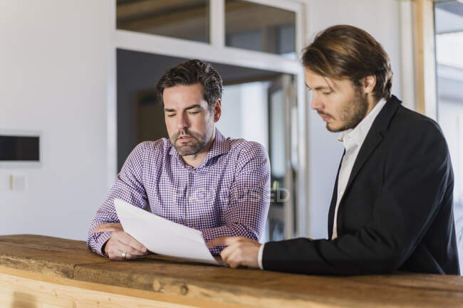 Два бізнесмени з документами розмовляють в дерев'яному офісі з відкритим плануванням — стокове фото