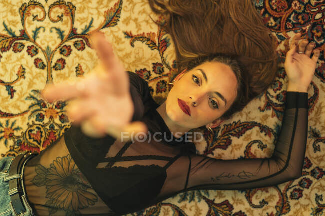 Portrait de jeune femme tatouée allongée sur le sol levant la main — Photo de stock