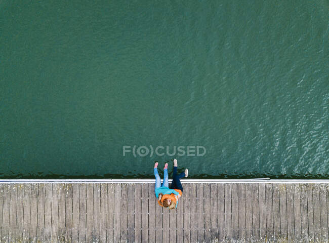Dos amigos felices sentados juntos en el embarcadero abrazándose, Valdemurio Reservoir, Asturias, España - foto de stock