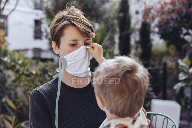 Littley boy ayudando a su madre a ponerse una máscara facial - foto de stock