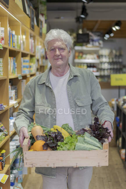 Portrait of senior man carrying crate with vegetables in a small food store — Stock Photo