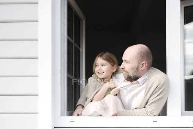 Зрілий чоловік з усміхненою донькою дивиться у вікно свого будинку. — стокове фото