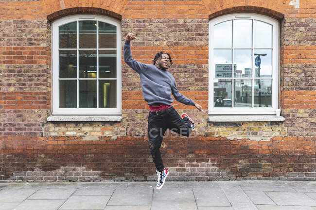 Young man jumping in front of brick wall — Stock Photo
