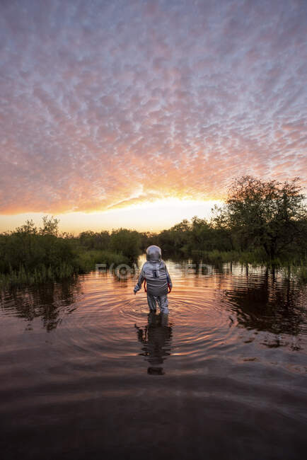 Spacewoman marche dans l'eau au coucher du soleil — Photo de stock