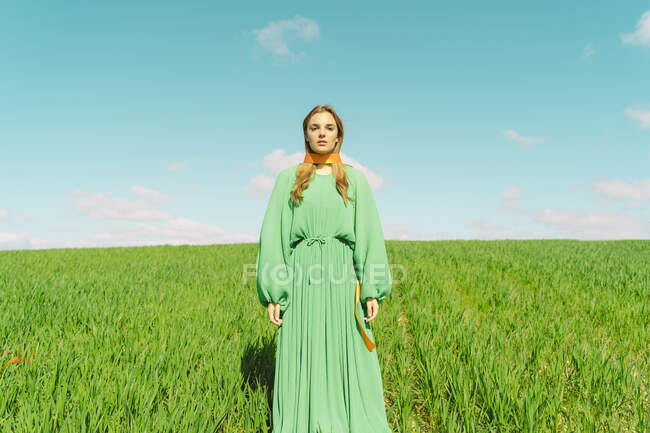 Ritratto di giovane donna che indossa un abito verde in piedi in un campo con un nastro intorno al collo — Foto stock