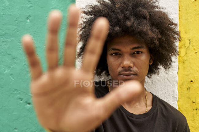Портрет молодого человека с афро, стоящего перед красочной стеной, поднимающей руку — стоковое фото