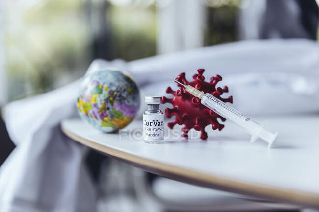 Modelo de coronavirus con vacuna sobre mesa con mini globo - foto de stock