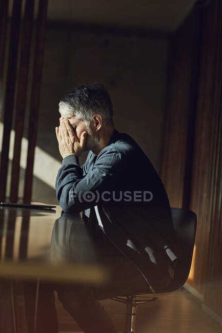 Hombre de negocios casual sentado en su oficina sostenible, cabeza en manos - foto de stock