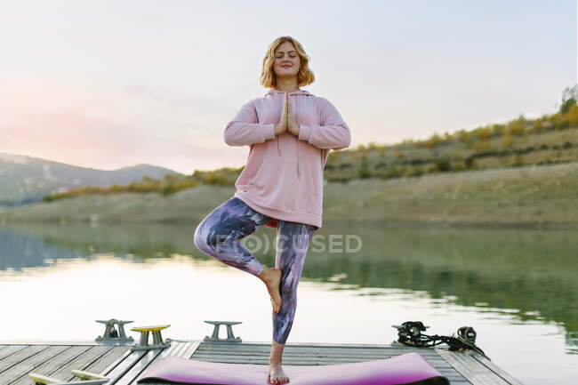 Giovane donna che fa yoga su un molo, posizione dell'albero — Foto stock