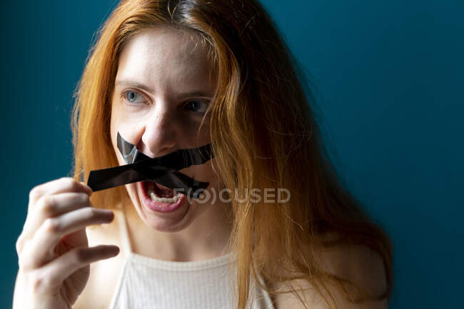 Ritratto di giovane donna urlante che tira fuori del nastro adesivo dalla bocca — Foto stock