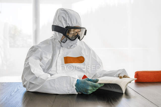 Mulher, vestindo roupas protetoras, sentada à mesa, livro de leitura — Fotografia de Stock