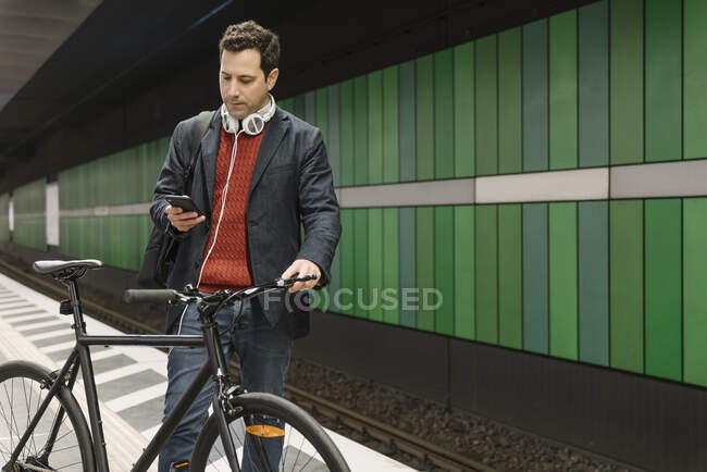 Businessman with bicycle text messaging on mobile phone while standing on subway station — Stock Photo