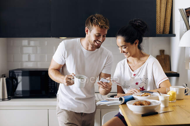 Feliz jovem casal na cozinha olhando para o telefone celular — Fotografia de Stock