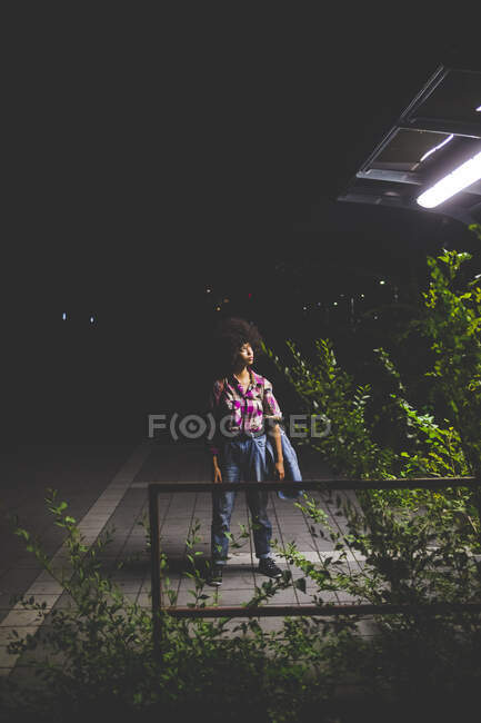 Mujer joven con peinado afro de pie en la plataforma por la noche - foto de stock