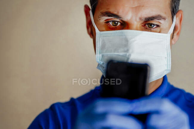 Médico con mascarilla facial, usando smartphone - foto de stock