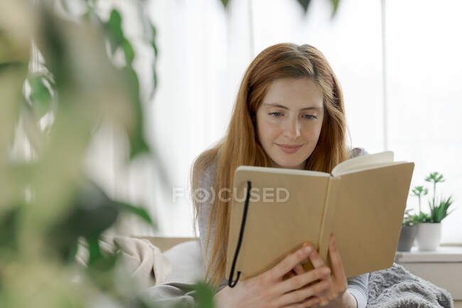 Mujer joven leyendo cuaderno en casa - foto de stock