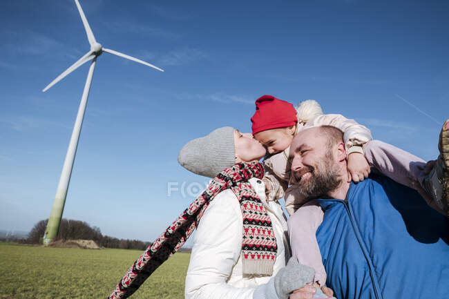 Padres felices con hija pequeña contra el cielo con rueda de viento en el fondo - foto de stock