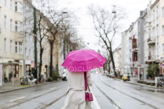 Vista trasera de una mujer con paraguas rosa caminando por la calle - foto de stock