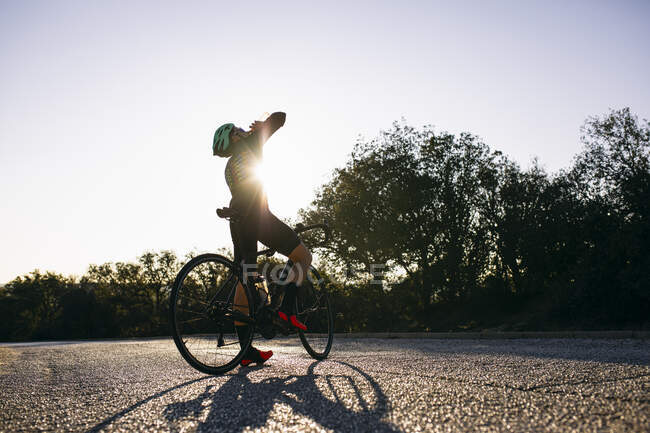 Cycliste buvant de la bouteille pendant une pause sur une route de campagne au coucher du soleil — Photo de stock