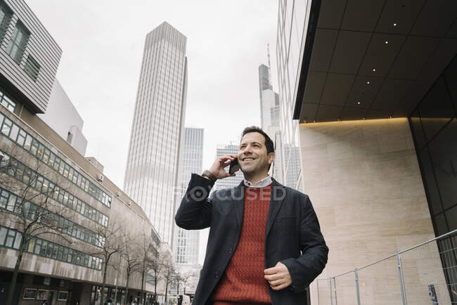 Уверенный в себе предприниматель, разговаривающий по мобильному телефону во время прогулки по городу, Франкфурт, Германия — стоковое фото