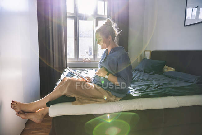Donna incinta sdraiata sul letto a casa con tablet — Foto stock