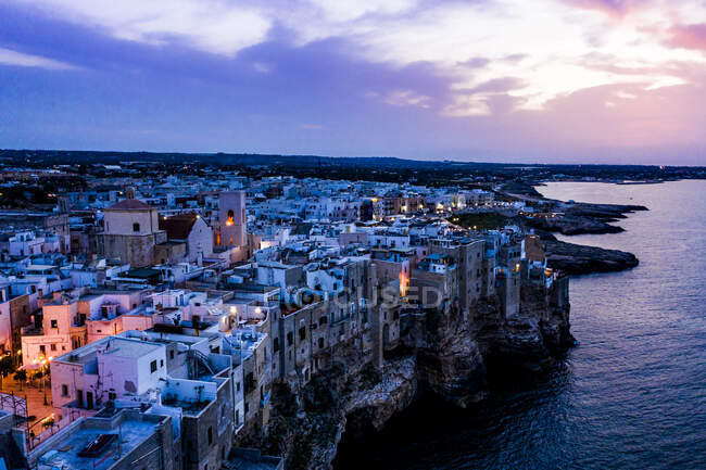 Italy, Polignano a Mare, Helicopter view of cliffs and buildings of coastal town at dusk — Stock Photo
