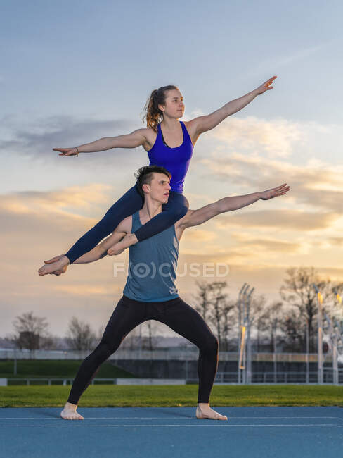 Jeune couple faisant des acrobaties au coucher du soleil — Photo de stock