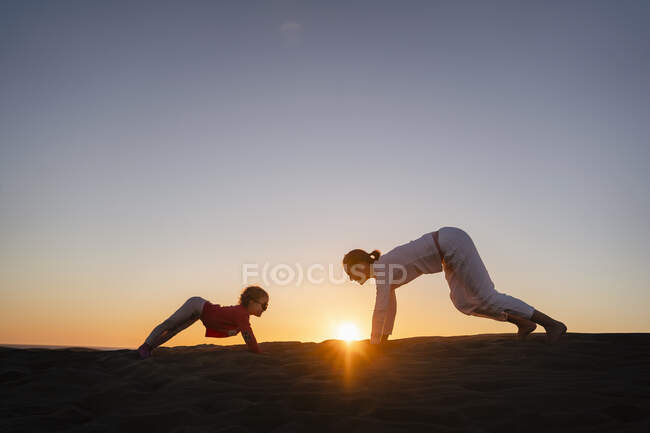 Mother and daughter practicing yoga in sand dunes at sunset, Gran Canaria, Spain — Stock Photo