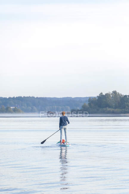 Femme debout sur la planche à soup le matin sur un lac — Photo de stock