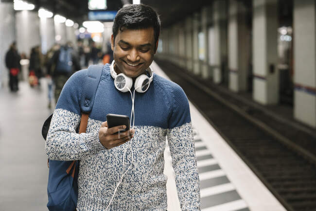 Улыбающийся человек с помощью смартфона на станции метро — стоковое фото