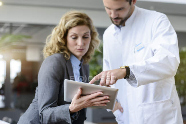 Mujer de negocios con tableta y médico hablando en el hospital - foto de stock