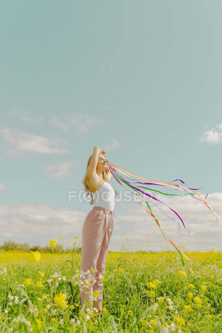 Mulher jovem com fitas coloridas em um prado de flor na primavera — Fotografia de Stock