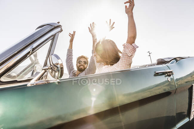 Happy couple with raised arms in convertible car on a road trip — Stock Photo