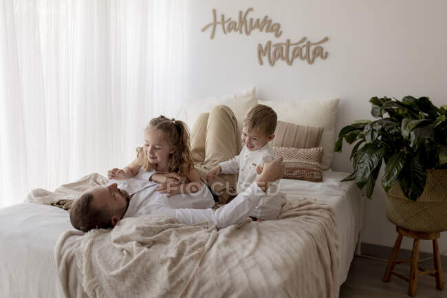 Padre sdraiato sul letto a giocare con i suoi due figli — Foto stock