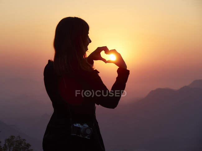 Silhouette di donna che plasma il cuore con le mani al tramonto, Serra da Leba, Angola — Foto stock