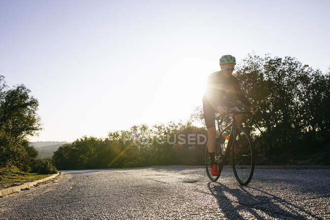 Atleta in bicicletta sulla strada di campagna al tramonto — Foto stock