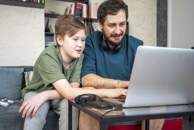 Portrait of father and son sitting together on the couch at home using laptop — Stock Photo
