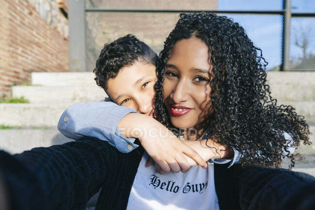 Retrato de madre e hijo felices sentados juntos en pasos tomando selfie - foto de stock