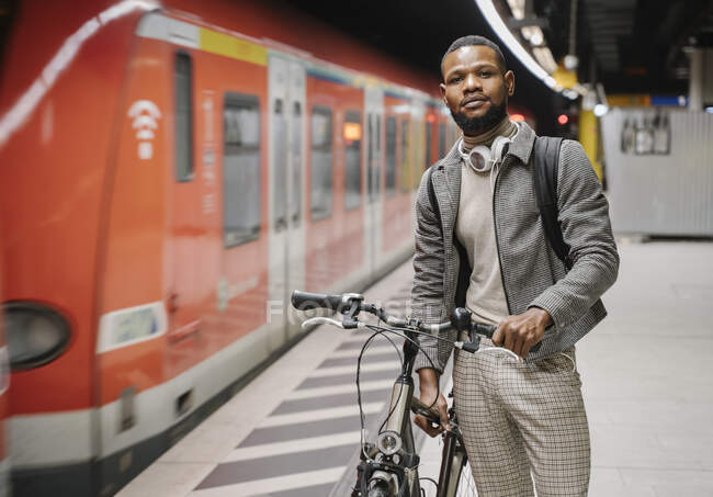Homem elegante com uma bicicleta e fones de ouvido em uma estação de metro — Fotografia de Stock