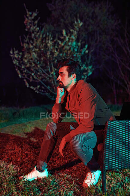 Вдумчивый человек, сидящий один на скамейке в саду ночью — стоковое фото