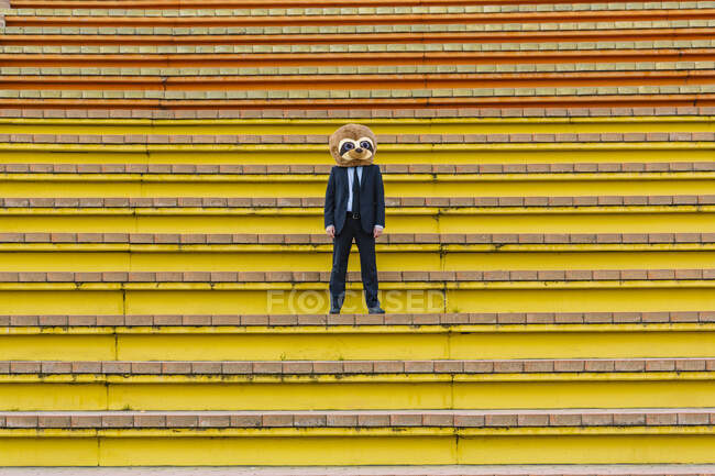 Businessman in black suit with meerkat mask standing on stairs — Stock Photo